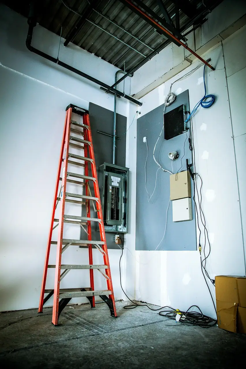 A ladder set up beside an open electrical panel and fresh wiring