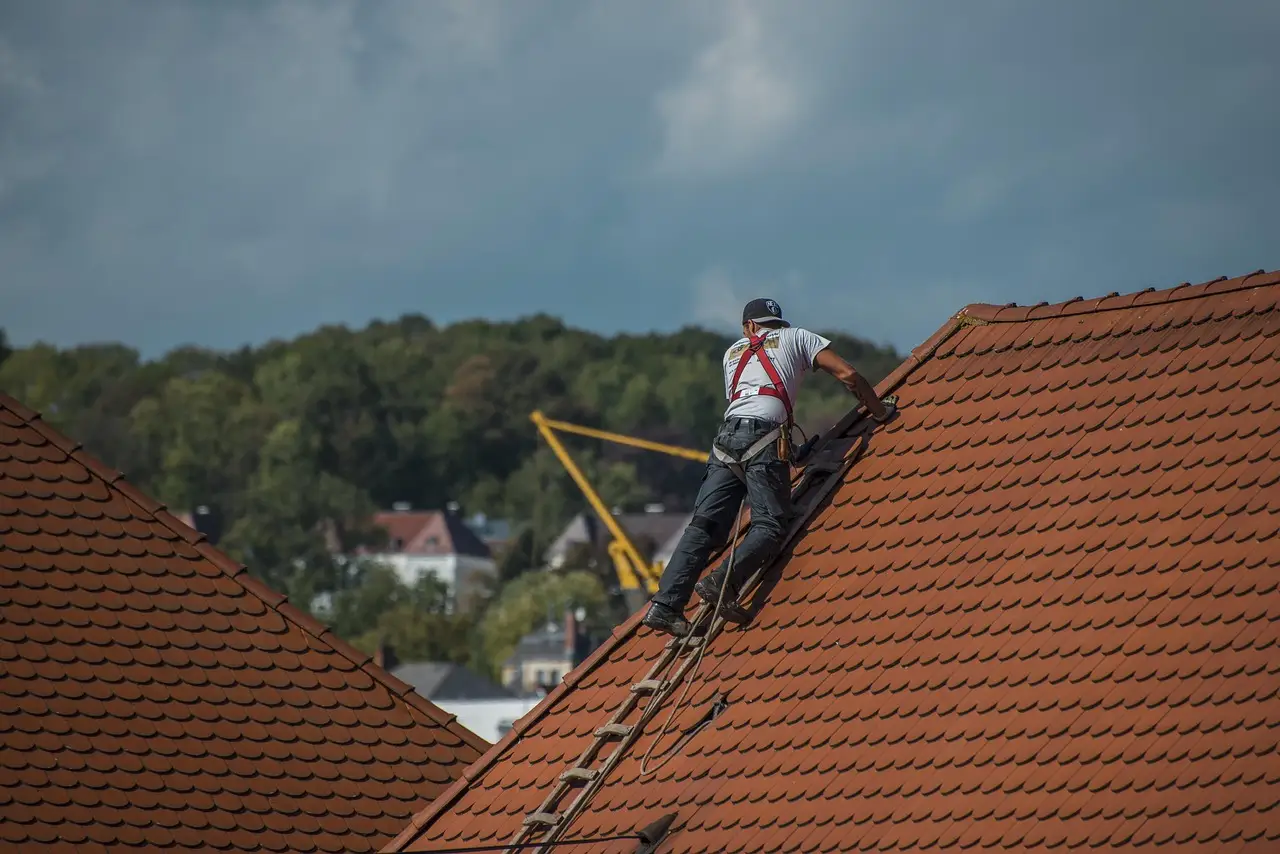 A roofer in a harness climbing a steep tile roof